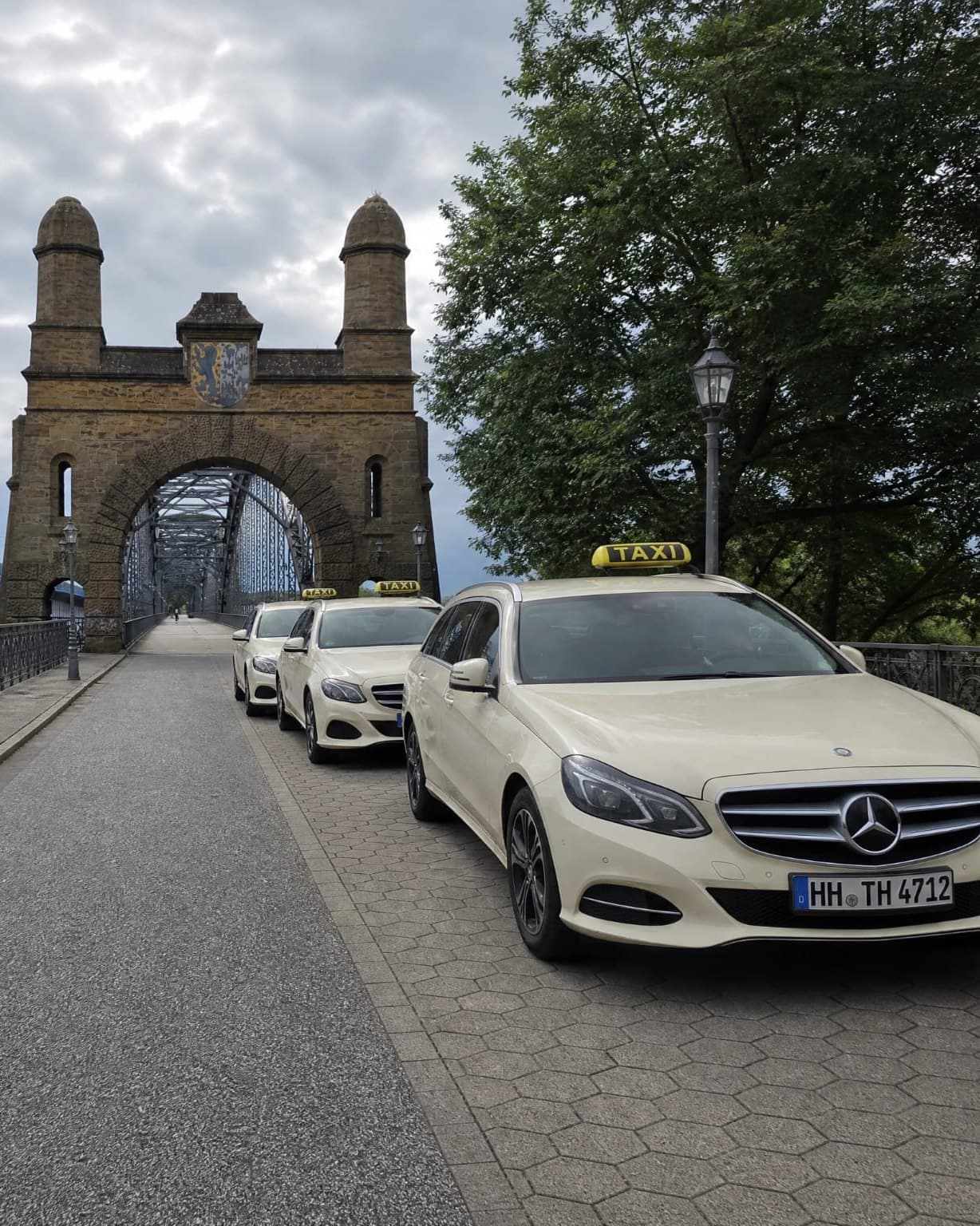 Drei helle Taxis stehen hintereinander auf der Alten Harburger Elbbrücke, dahinter das steinerne Brückentor mit zwei Türmen